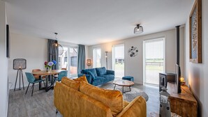A modern living room with a sofa, a dining table, and a TV. - Holiday home near forest with wellness garden (Den Burg)