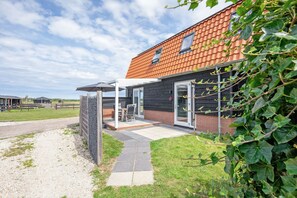 Een modern huis met een bakstenen gevel, een overdekte patio met tuinmeubilair en een heldere lucht.