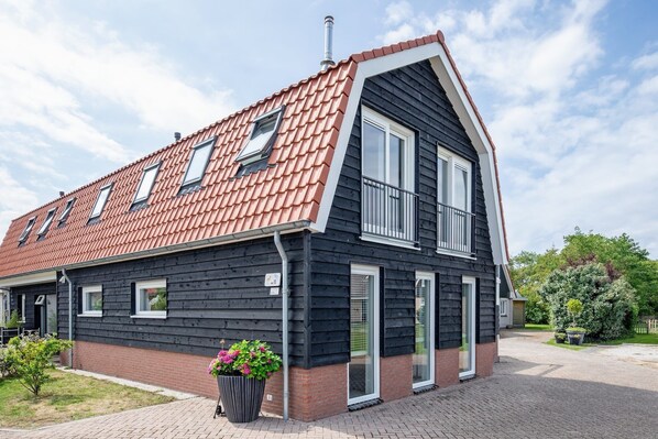 Een huis met twee verdiepingen, voorzien van een rode dakbedekking, zwarte bekleding en een klein balkon.