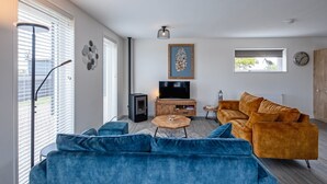 A modern living room with a blue sofa, a wooden coffee table, and a TV on a wooden cabinet. - Holiday home near forest with wellness garden (Den Burg)
