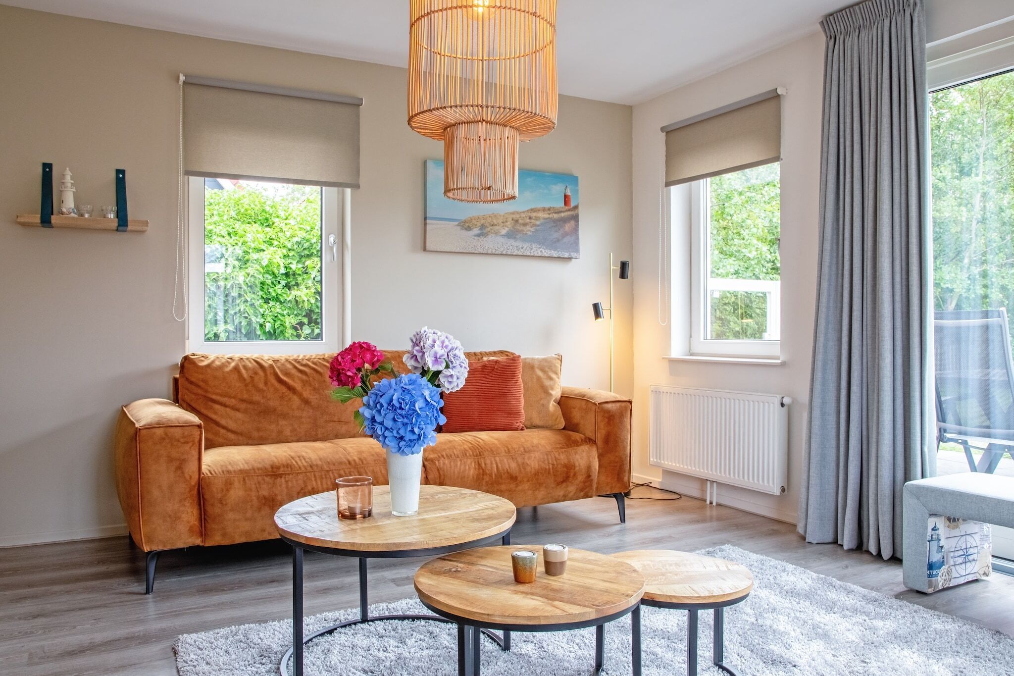 Ein modernes Wohnzimmer mit einem braunen Sofa, zwei runden Couchtischen und einem großen Fenster mit Vorhängen.