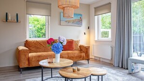 A modern living room with a brown sofa, two round coffee tables, and a large window with curtains.