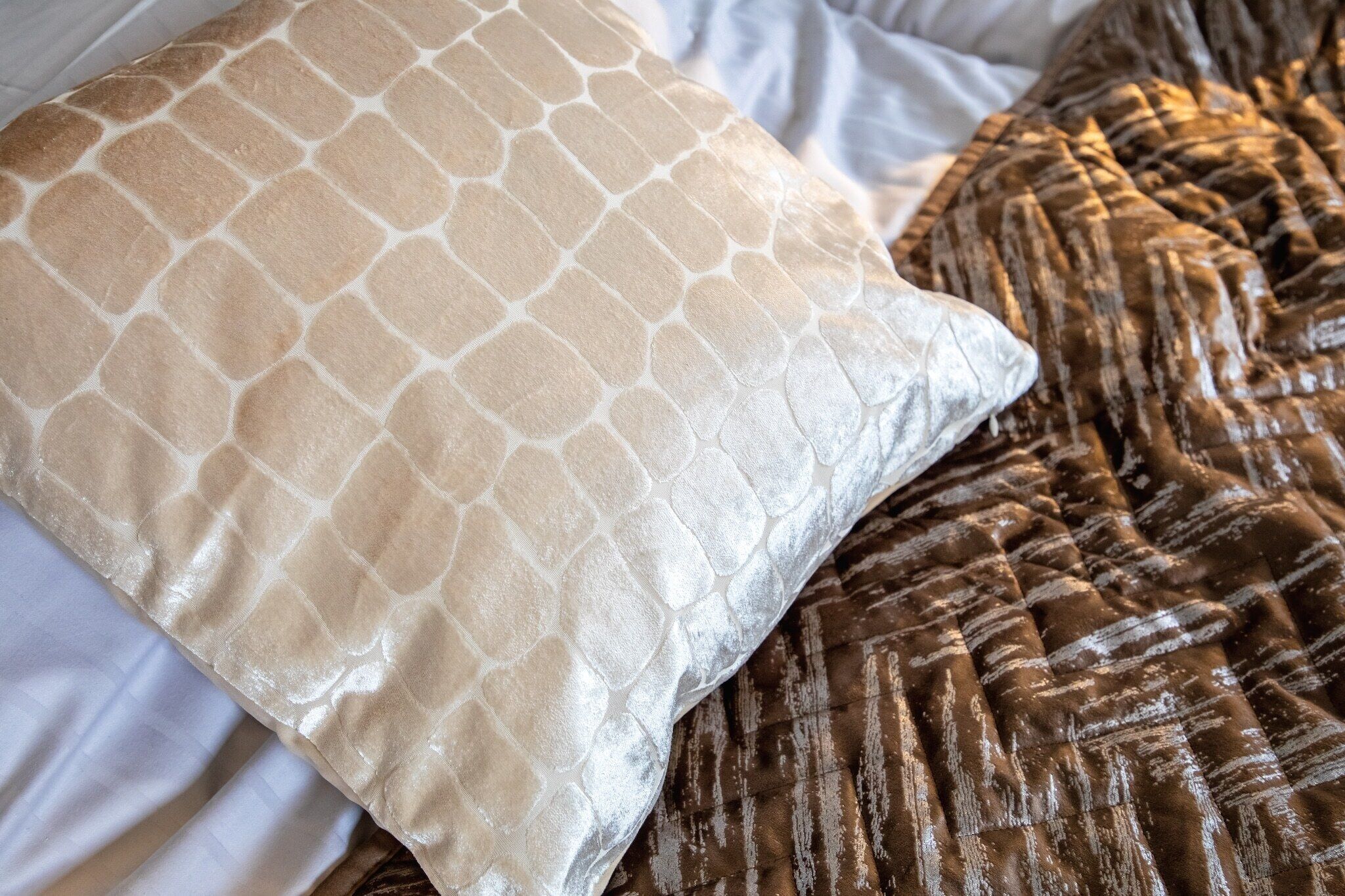 A bed with a patterned pillow and a textured blanket.