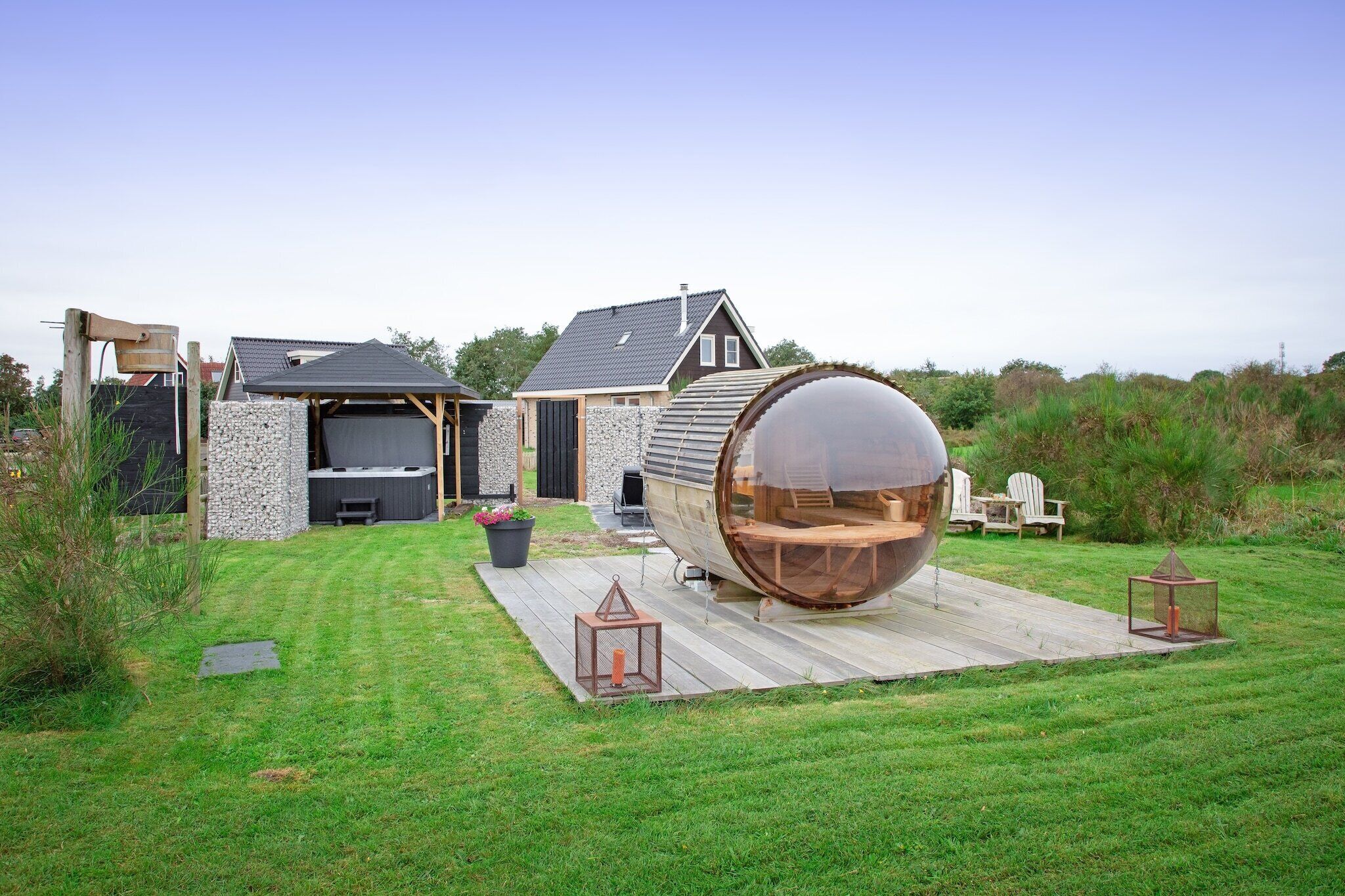 A modern house with a large wooden barrel structure in the backyard, a stone wall, and a wooden deck.