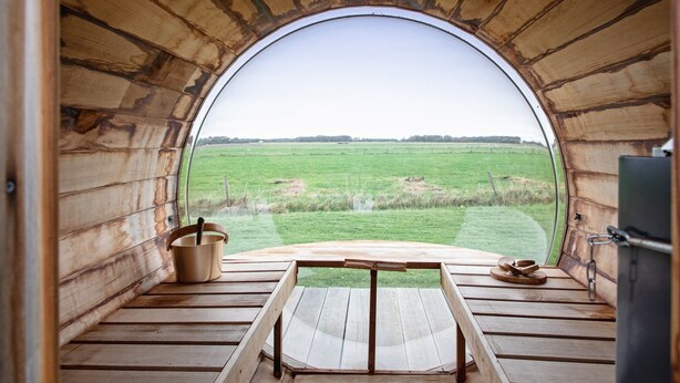 A wooden interior with a large arched window overlooking a green field.