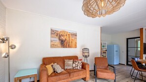 A living room with a brown sofa, a blue chair, a round coffee table, and a floor lamp. - Cozy holiday home in Den Burg with hot tub (Den Burg)