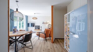 A modern living room with a wooden dining table, orange chairs, and a hanging light fixture. - Cozy holiday home in Den Burg with hot tub (Den Burg)