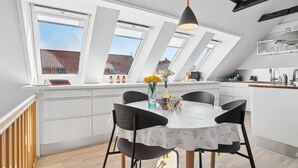 Eine moderne Küche mit Dachfenstern, weißen Schränken und einem Essbereich mit Tisch und Stühlen.