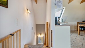 Een hal met een houten trap, een lijst met een afbeelding en een keuken met een aanrecht en apparatuur.