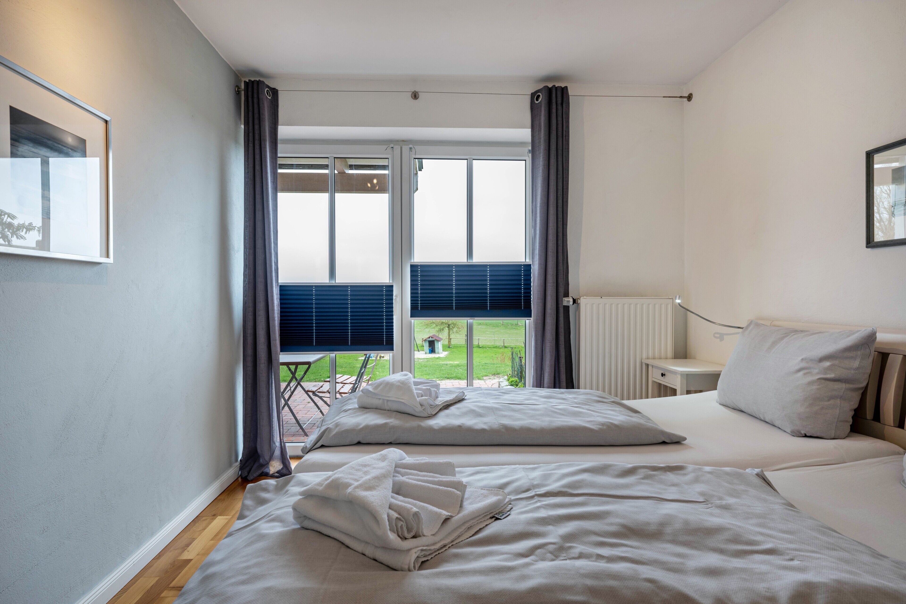 A bedroom with two beds, a window with curtains, a radiator, and a small table.