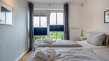A bedroom with two beds, a window with curtains, a radiator, and a small table.