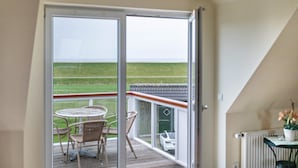 Een balkon met uitzicht op een groen veld, een witte auto en een tafel met stoelen.