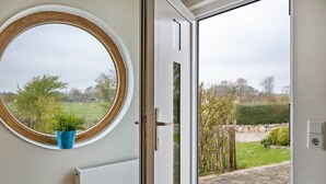 Een kamer met een groot rond raam, een witte deur en uitzicht op een tuin.