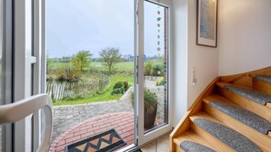 Une pièce avec un escalier en bois, une grande fenêtre donnant sur un jardin et un tableau encadré accroché au mur.