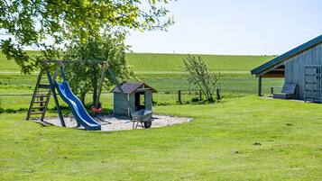 A playground with a slide and swing set, a small shed, and a barn-like structure in a grassy field.