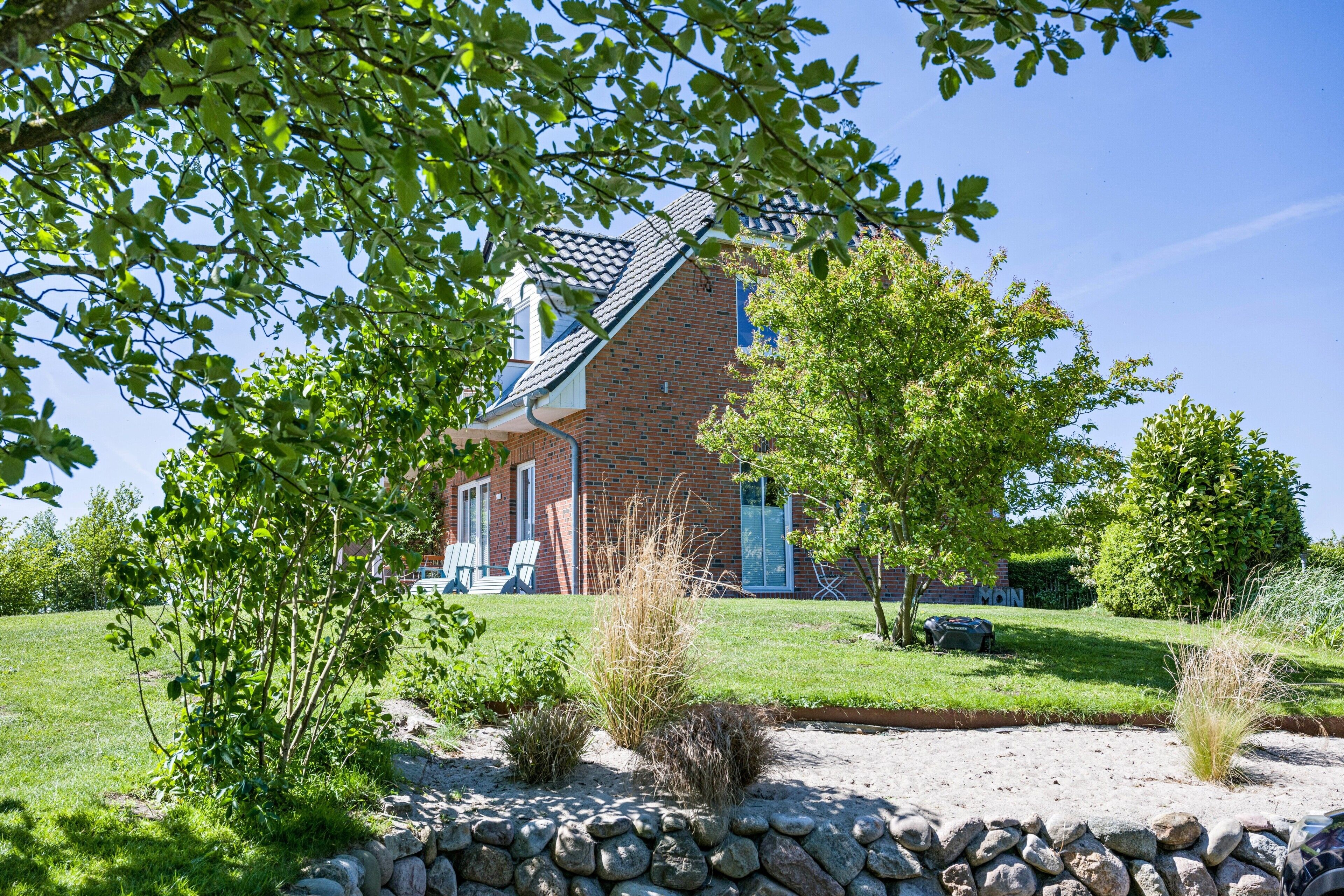A brick house with a sloped roof, surrounded by a well-maintained lawn and a stone wall.