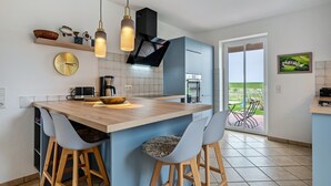Une cuisine moderne dotée d’un îlot central, de tabourets de bar, de luminaires suspendus et offrant une vue sur l’extérieur.