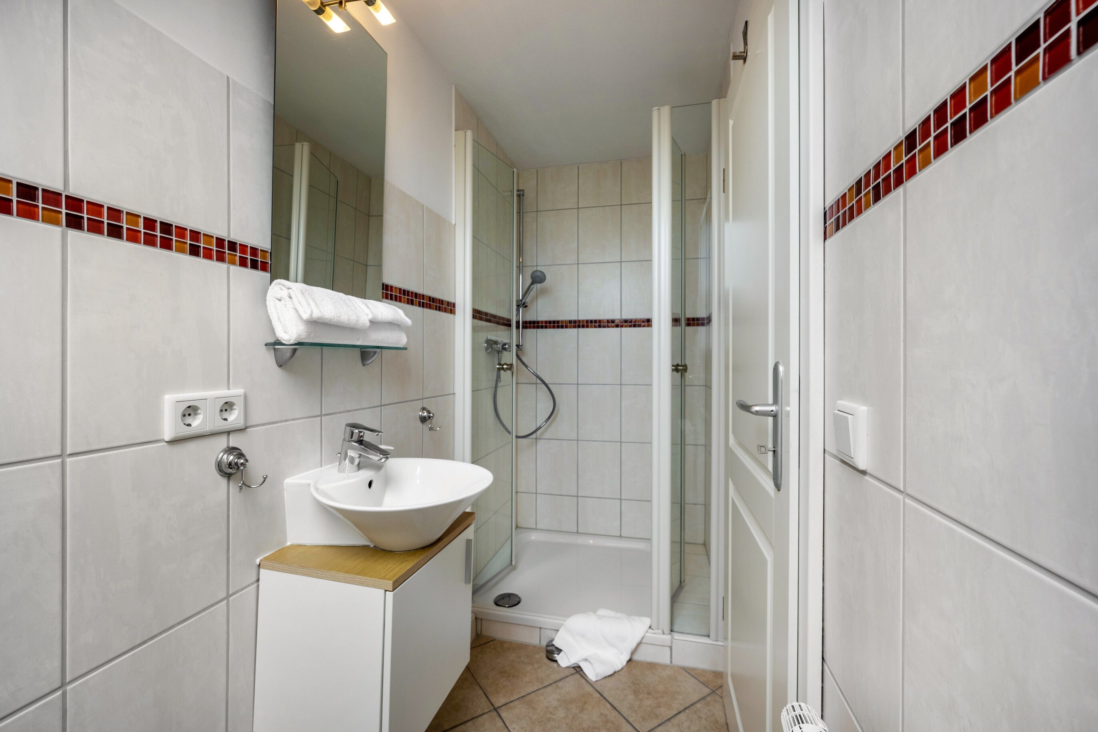 Une salle de bain avec un lavabo, un miroir, une douche et des murs carrelés.
