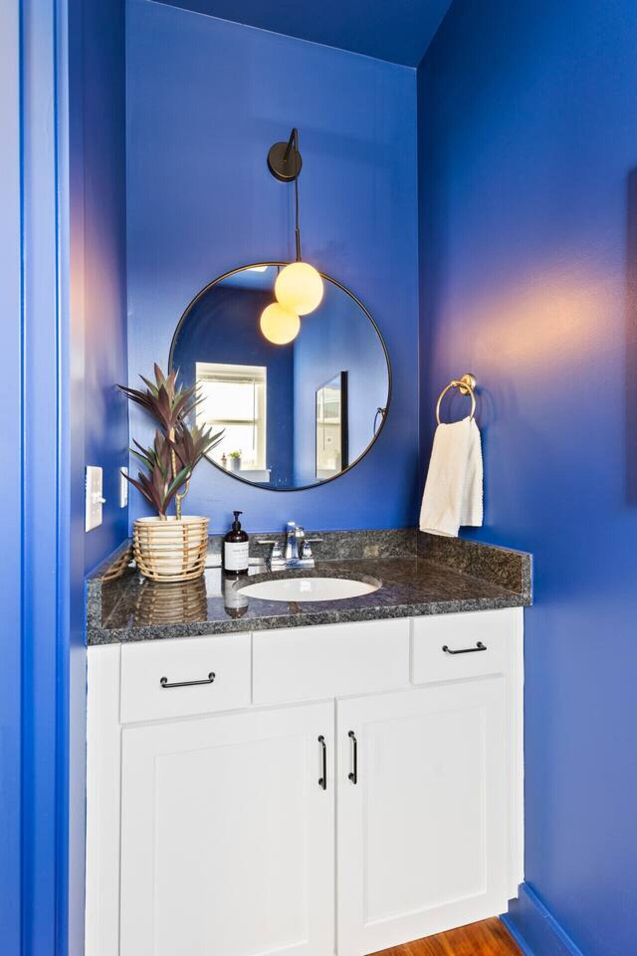 A bathroom with a blue wall, white cabinets, a round mirror, a sink, and a towel hanging on the wall.
