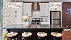 A modern kitchen with white cabinetry, a central island with stools, stainless steel appliances, and pendant lighting.