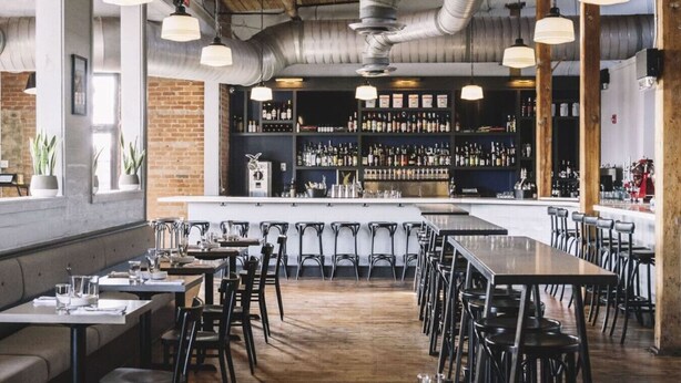 A modern bar with a long counter, multiple seating areas, and exposed ductwork on the ceiling.