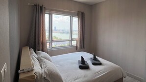 A hotel room with a large bed, a window with curtains, a view of the city, and a ceiling light. - River view pool gym train market wifi (Nonthaburi)