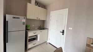 A compact kitchen with a stainless steel refrigerator, a microwave, and a sink. There is a white door with a handle and a small cabinet above the sink. - River view pool gym train market wifi (Nonthaburi)
