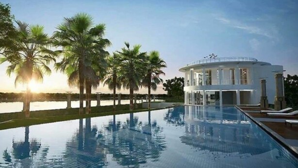 A poolside view of a hotel with a circular building, palm trees, and a clear sky. - River view pool gym train market wifi (Nonthaburi)
