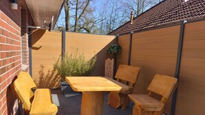 A wooden outdoor seating area with a table and chairs, a brick wall, and a wooden fence. - Modern vacation home with terrace in a quiet cul-de-sac in beautiful Aurich (Aurich)
