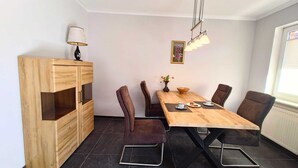 A modern dining area with a wooden table, black chairs, a vase with flowers, and a lamp on a cabinet. - Modern vacation home with terrace in a quiet cul-de-sac in beautiful Aurich (Aurich)