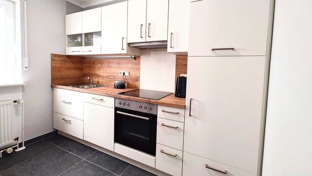 A modern kitchen with white cabinets, a wooden countertop, a built-in oven, and a refrigerator. - Modern vacation home with terrace in a quiet cul-de-sac in beautiful Aurich (Aurich)
