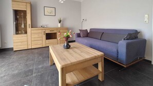 A modern living room with a wooden coffee table, a sofa, a cabinet with glass doors, and a pendant light. - Modern vacation home with terrace in a quiet cul-de-sac in beautiful Aurich (Aurich)