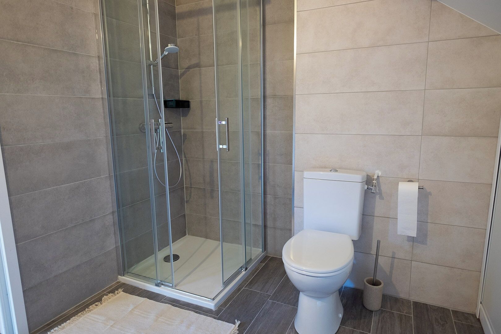 A modern bathroom with a glass-enclosed shower, a white toilet, and a beige tiled floor.