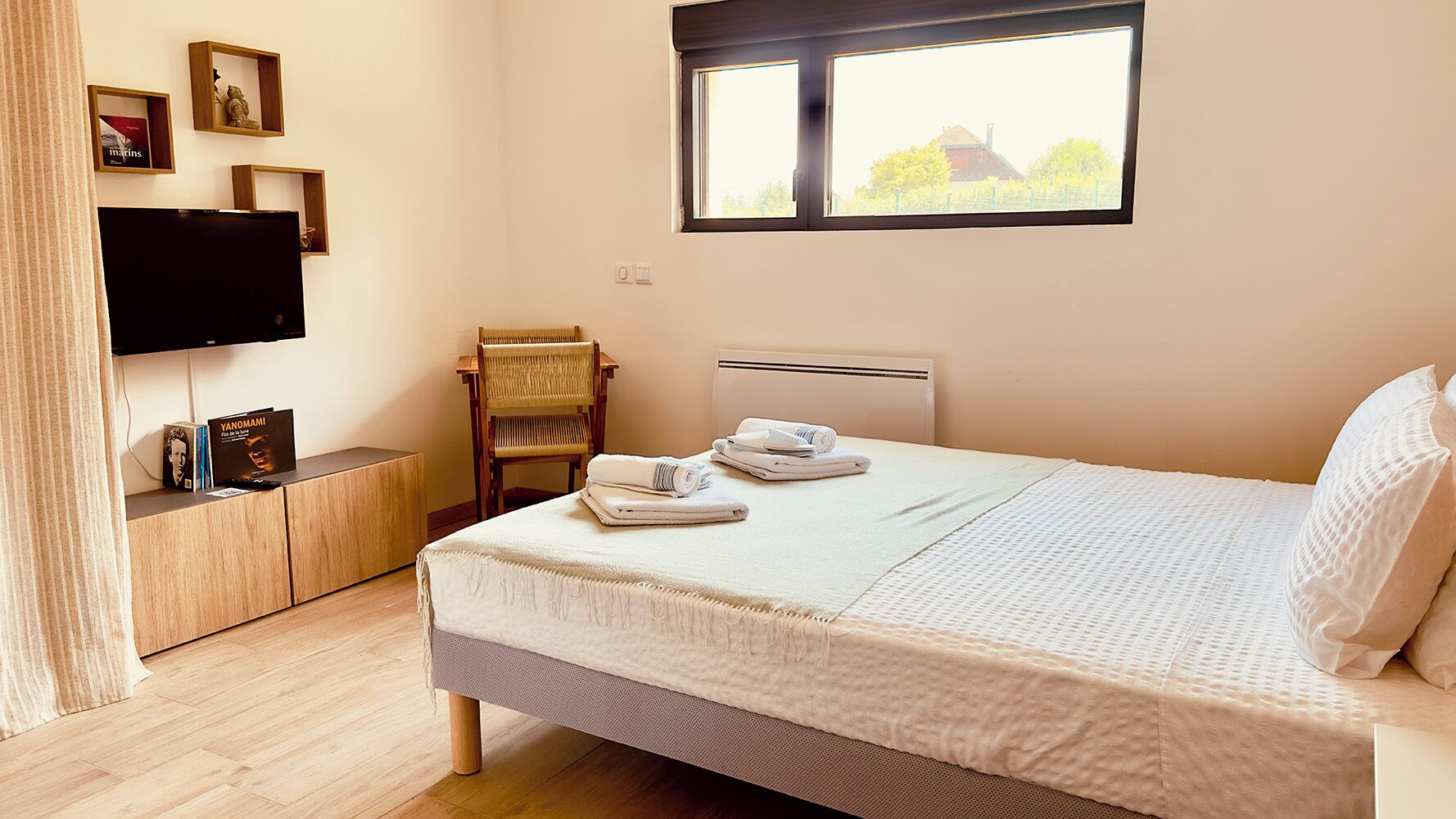 A bedroom with a bed, a chair, a TV, and a window.