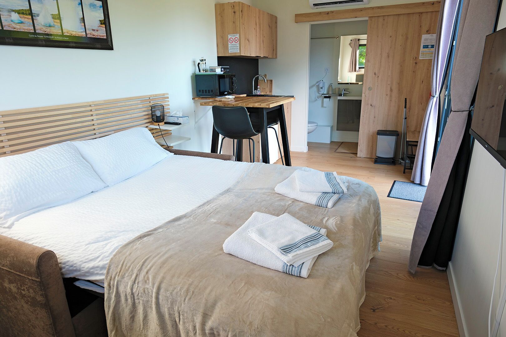 Ein Schlafzimmer mit einem Bett, zwei Handtüchern, einem Schreibtisch mit Stuhl, einer Mikrowelle und einer kleinen Küche.