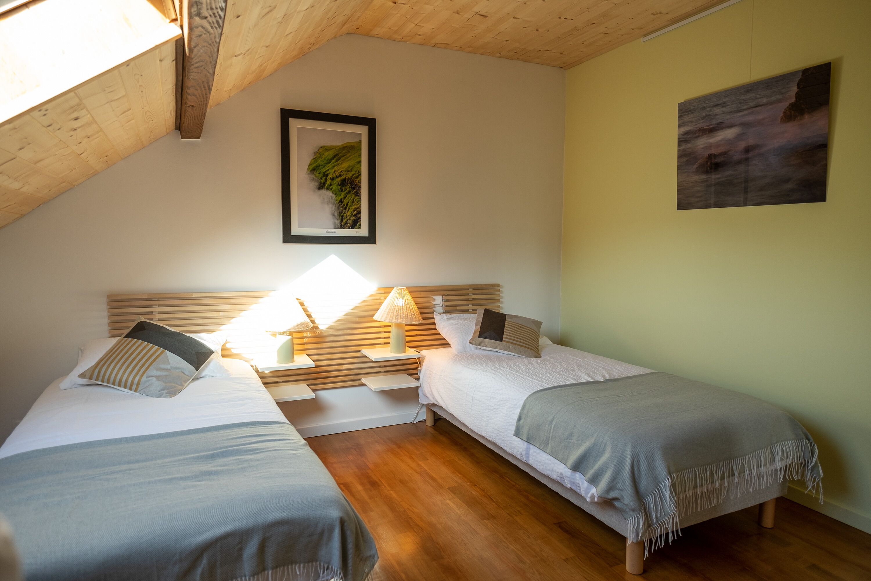 Una habitación con dos camas, cabeceros de madera, un cuadro en la pared y una lámpara en la mesita de noche.
