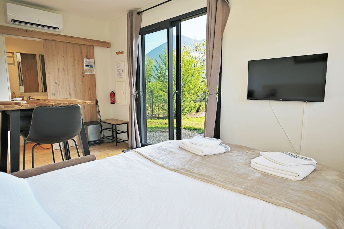 Habitación de hotel con cama, escritorio, silla, televisor y vistas a zonas verdes y montañas.