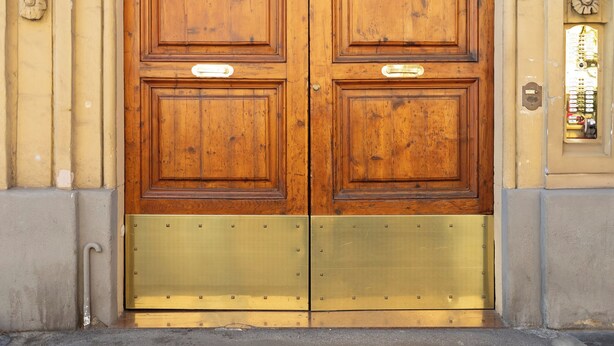 A double wooden door with a brass threshold, a number '54' on the wall, and a small window with a view of the street. - Style & Stone Guest House (Rome)