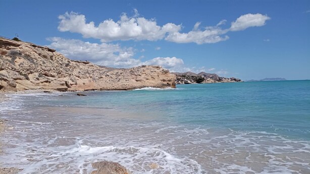 A beach with clear turquoise water, rocky terrain, and a distant view of a town. - Villa Garden, Pool & sea (El Campello)