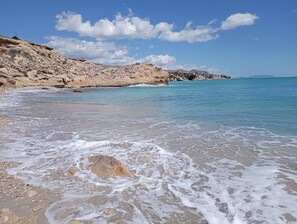 A beach with clear turquoise water, rocky terrain, and a distant view of a town. - Villa Garden, Pool & sea (El Campello)