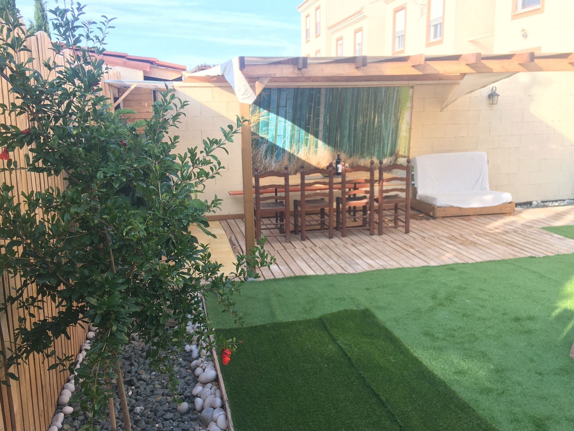 Un patio con un tavolo e sedie di legno, un divano bianco e un prato sintetico verde.