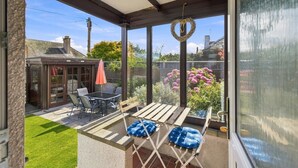 A covered patio with a table and chairs, a bench, and a small garden area with flowers.