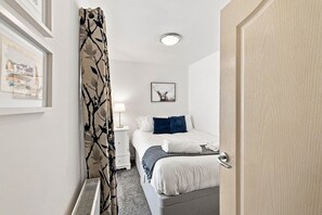 A hotel room with a bed, a bedside table, a lamp, and a framed picture on the wall.