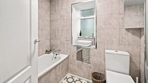 A bathroom with a white bathtub, a sink, and a toilet. There is a window with frosted glass and a mirror above the sink.