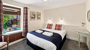 A bedroom with a bed, a window with curtains, a bedside table, and a wall-mounted light fixture.