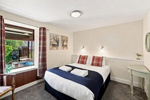 A bedroom with a bed, a window with curtains, a bedside table, and a wall-mounted light fixture.