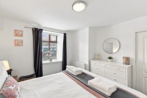 A bedroom with a bed, a dresser, a mirror, and a window with curtains.