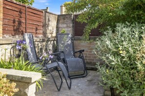 A patio with two chairs, a stone wall, and a wooden fence.