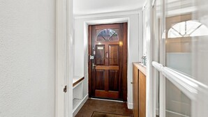 A hallway with a wooden door, a white wall, and a window with blinds.