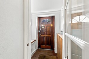 Un pasillo con puerta de madera, pared blanca y ventana con persianas.